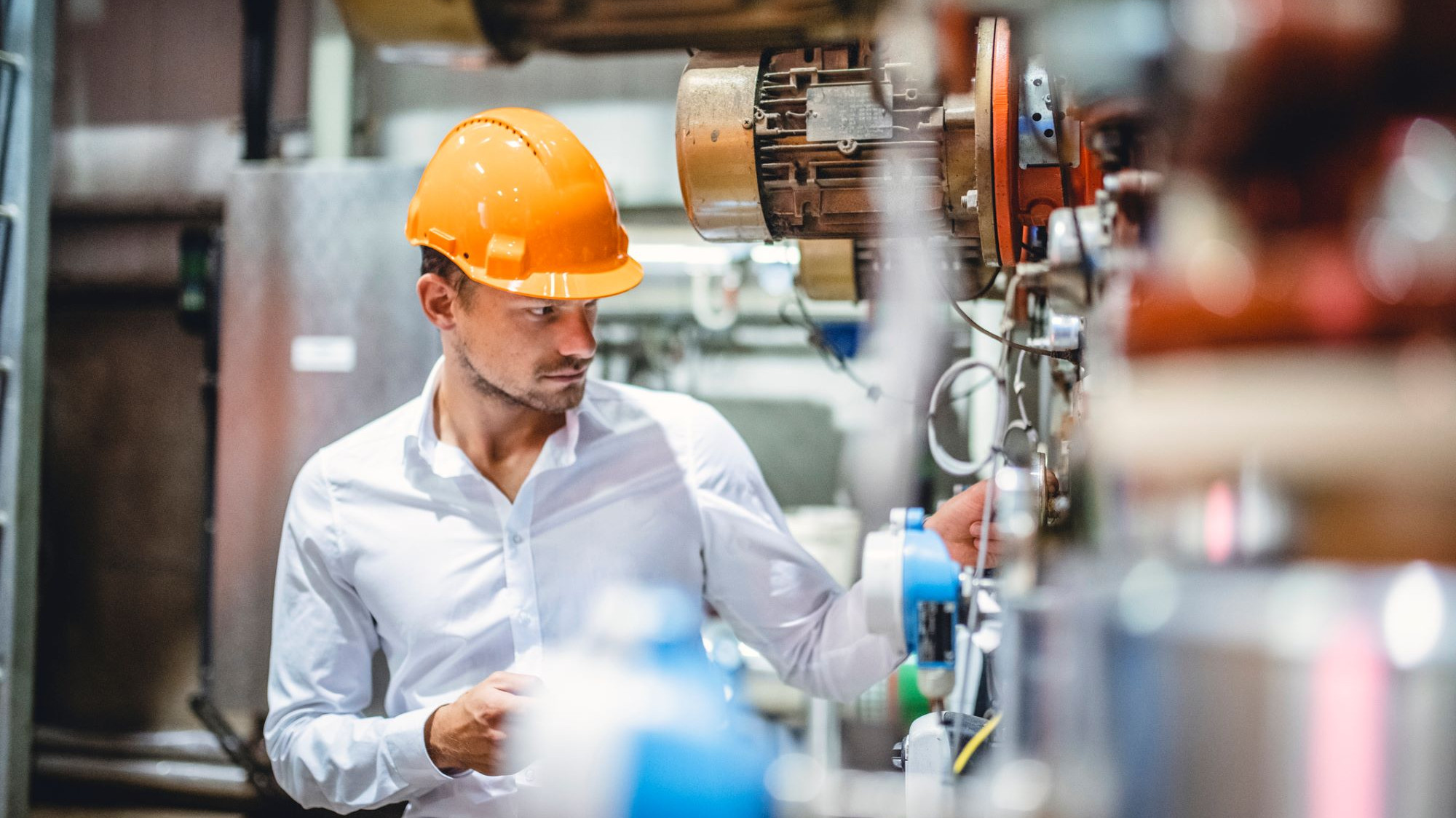 Bild: Arbeiter mit Helm steht an einer Maschine